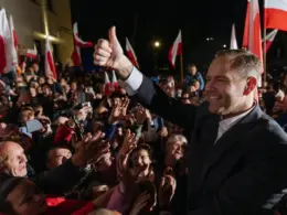 Karol Nawrocki gives a thumbs-up to a crowd waving Polish flags on his presidential election night.