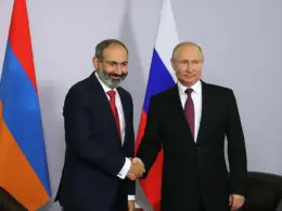 Armenian Prime Minister Nikol Pashinyan shakes hands with Russian President Vladimir Putin in front of Armenian and Russian flags during a bilateral meeting.
