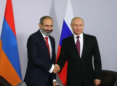 Armenian Prime Minister Nikol Pashinyan shakes hands with Russian President Vladimir Putin in front of Armenian and Russian flags during a bilateral meeting.