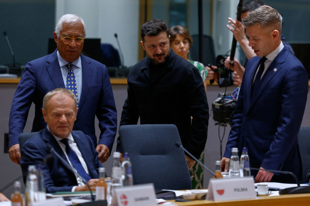 Zelenskyy, Magyar, Tusk, and Costa confer around a table during an EU meeting, with one official in black standing at the center.