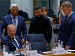 Zelenskyy, Magyar, Tusk, and Costa confer around a table during an EU meeting, with one official in black standing at the center.