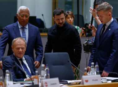 Zelenskyy, Magyar, Tusk, and Costa confer around a table during an EU meeting, with one official in black standing at the center.