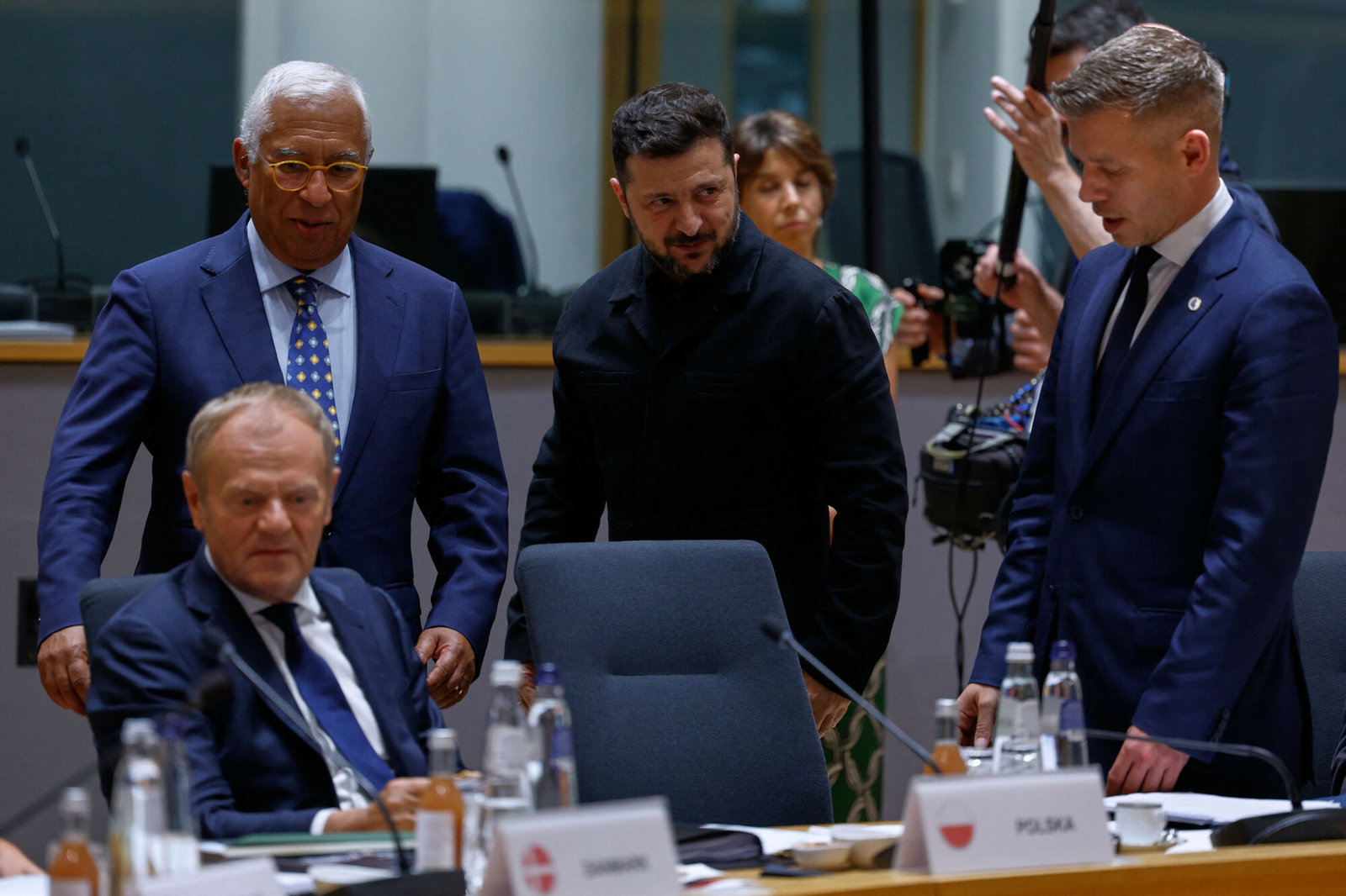 Zelenskyy, Magyar, Tusk, and Costa confer around a table during an EU meeting, with one official in black standing at the center.