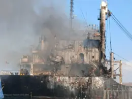 Smoke rises from the burned and heavily damaged superstructure of the Golden Leo cargo ship at sea.