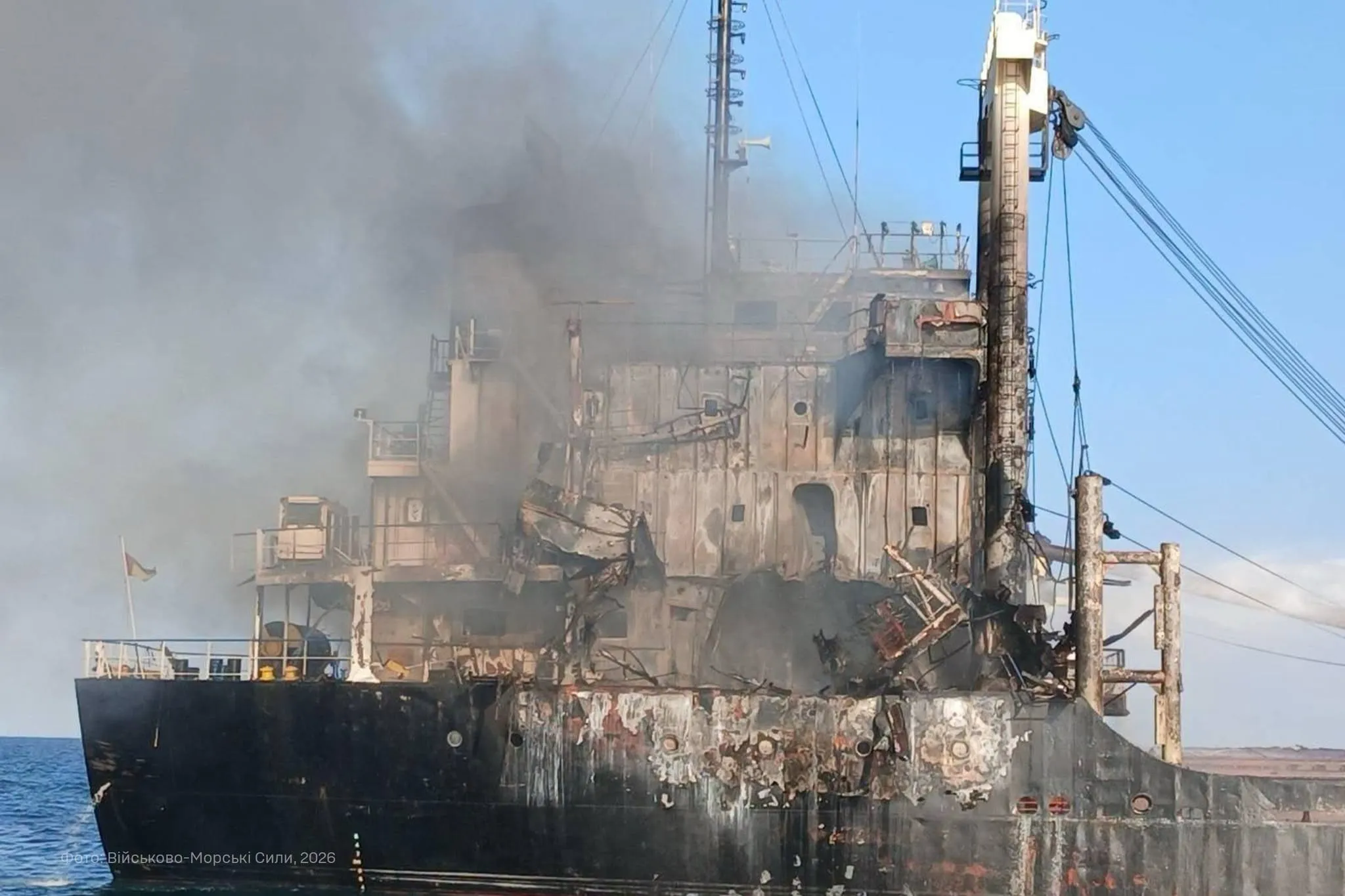 Smoke rises from the burned and heavily damaged superstructure of the Golden Leo cargo ship at sea.
