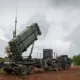 A Patriot air defense launcher raised into firing position on a military trailer.