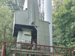 Close-up of equipment at the base of a communications tower behind a metal fence in a wooded area.
