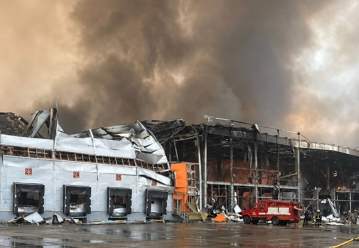 Firefighters beside a heavily damaged warehouse holding Bosch products as smoke rises from its collapsed roof.
