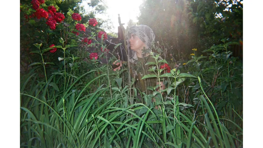A Ukrainian servicewoman poses among tall grass and flowers near a frontline position, 2025. Photo: project participant Kseniia “Jane”