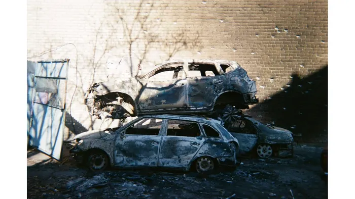 Burned-out vehicles stand beside a damaged building after an attack, 2025. Photo: project participant Viktor Holikov
