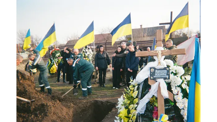 Mourners attend the funeral of a fallen Ukrainian service member, surrounded by Ukrainian flags and wreaths, 2025. Photo: project participant Viktor Holikov