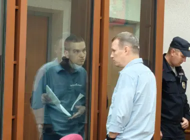 Ivan Stolbov stands behind glass in a Russian courtroom beside a man and a uniformed guard.