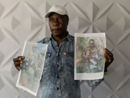 A Kenyan man holds two printed photographs of his son killed fighting for Russia.