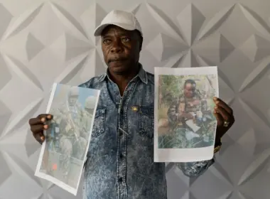 A Kenyan man holds two printed photographs of his son killed fighting for Russia.