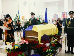 A priest conducts a memorial service beside Yevhen Konovalets’ flag-draped coffin, surrounded by flowers and an honor guard in Kyiv.