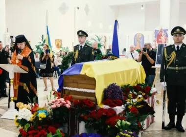 A priest conducts a memorial service beside Yevhen Konovalets’ flag-draped coffin, surrounded by flowers and an honor guard in Kyiv.