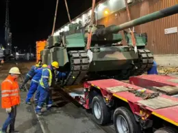 Workers unload a South Korean-made K2 Black Panther tank for the Polish army from a trailer at a Polish port at night.