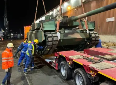 Workers unload a South Korean-made K2 Black Panther tank for the Polish army from a trailer at a Polish port at night.