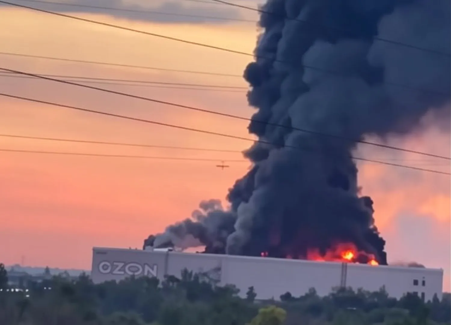 Thick black smoke and flames rise from an Ozon warehouse in Chapayevsk, Russia, at sunset.