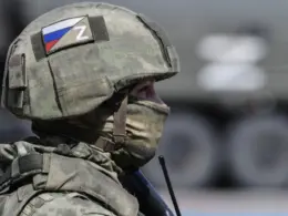 Russian soldier in camouflage wearing a helmet marked with the Russian flag and “Z” symbol.