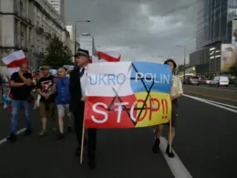 Demonstrators carrying Polish flags march behind a banner in Polish and Ukrainian colors reading “UKRO POLIN STOP!!” with a crossed-out Star of David.
