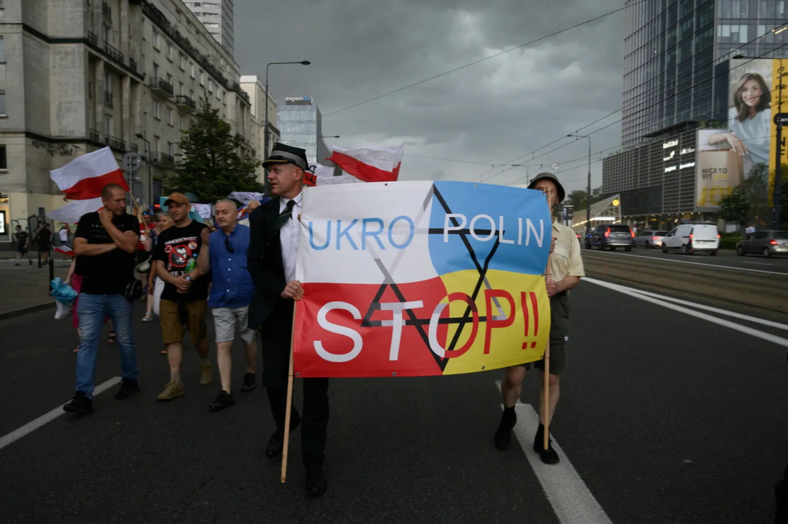 Demonstrators carrying Polish flags march behind a banner in Polish and Ukrainian colors reading “UKRO POLIN STOP!!” with a crossed-out Star of David.