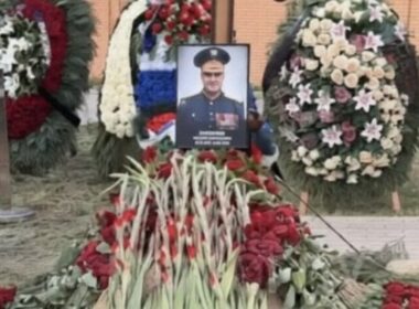 Portrait of Major General Valery Plokhotnyuk surrounded by red flowers and funeral wreaths at his burial site.