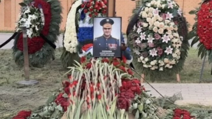 Portrait of Major General Valery Plokhotnyuk surrounded by red flowers and funeral wreaths at his burial site.