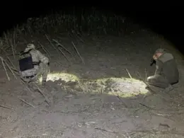 Two investigators examine a blast site with flashlights in a cornfield near Talmaza, Moldova, at night.