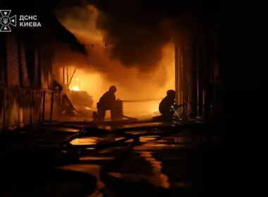 Three firefighters work amid flames and thick smoke at night.