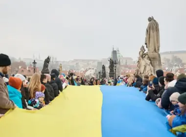 People line Prague’s Charles Bridge holding a long Ukrainian flag, with Prague Castle visible in the background.