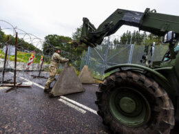 Lithuanian soldier installs concrete barriers and razor wire across a road during a civil defense exercise.