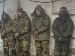Four captured fighters who fought for Russia stand against a wall with their hands bound.