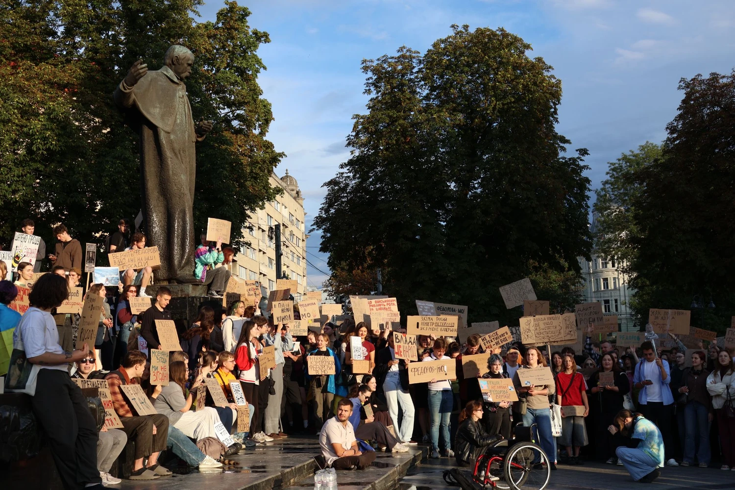 Demonstrators beneath the Taras Shevchenko monument in Lviv hold handwritten cardboard signs during an open-ended protest calling for Mykhailo Fedorov's reinstatement as Ukraine's Minister of Defence. Photo: Solomiia Stanovych/Euromaidan Press.