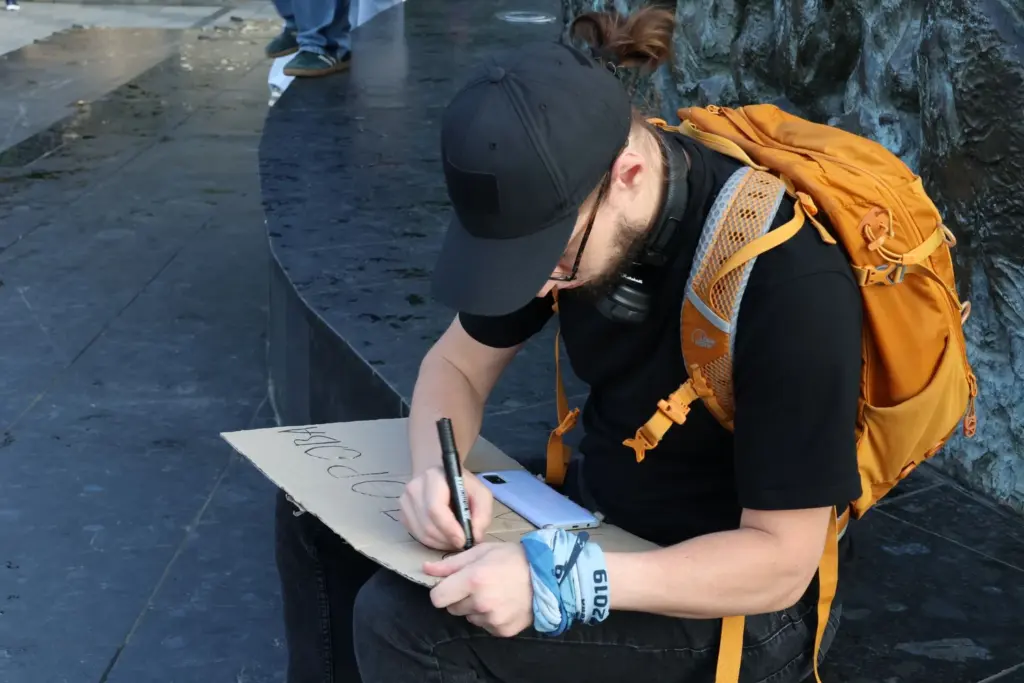 A protester prepares a handwritten cardboard sign before joining the demonstration calling for Mykhailo Fedorov's reinstatement as Minister of Defence. Photo: Euromaidan Press.