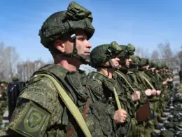 Russian soldiers in camouflage uniforms and helmets stand in formation outdoors.