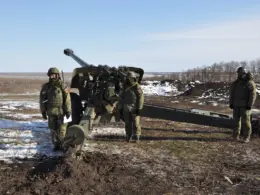 Russian soldiers stand beside a field artillery gun in a snow-covered position.