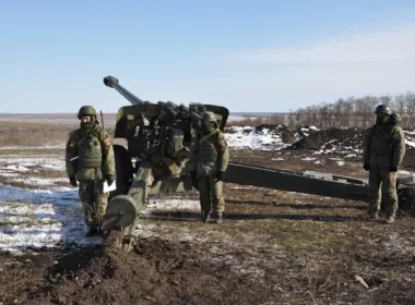 Russian soldiers stand beside a field artillery gun in a snow-covered position.