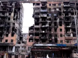 War-damaged apartment blocks in Mariupol with burned facades, shattered windows and exposed interiors.