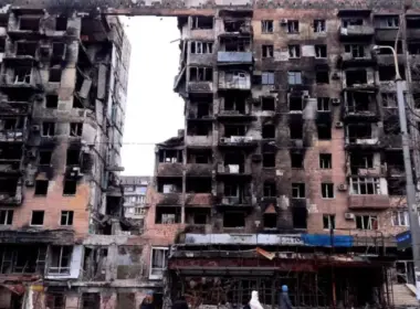 War-damaged apartment blocks in Mariupol with burned facades, shattered windows and exposed interiors.