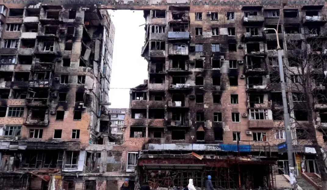War-damaged apartment blocks in Mariupol with burned facades, shattered windows and exposed interiors.