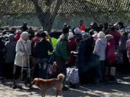 Residents, many elderly and carrying shopping trolleys, gather outdoors in occupied Oleshky, Kherson Oblast.