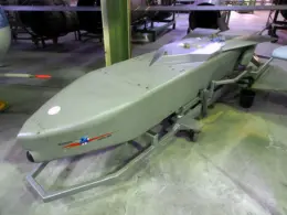 A gray Taurus KEPD 350 cruise missile displayed on a wheeled stand inside an exhibition hall.