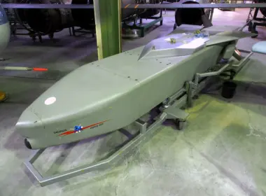 A gray Taurus KEPD 350 cruise missile displayed on a wheeled stand inside an exhibition hall.