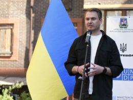 Ruslan Kravchenko speaks beside a large Ukrainian flag at a housing-rehabilitation event in Irpin in June 2023.