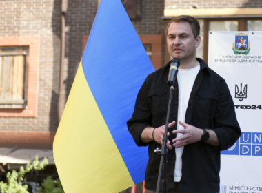 Ruslan Kravchenko speaks beside a large Ukrainian flag at a housing-rehabilitation event in Irpin in June 2023.