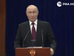Vladimir Putin stands behind a lectern during a press conference, with the RIA Novosti logo visible above him.
