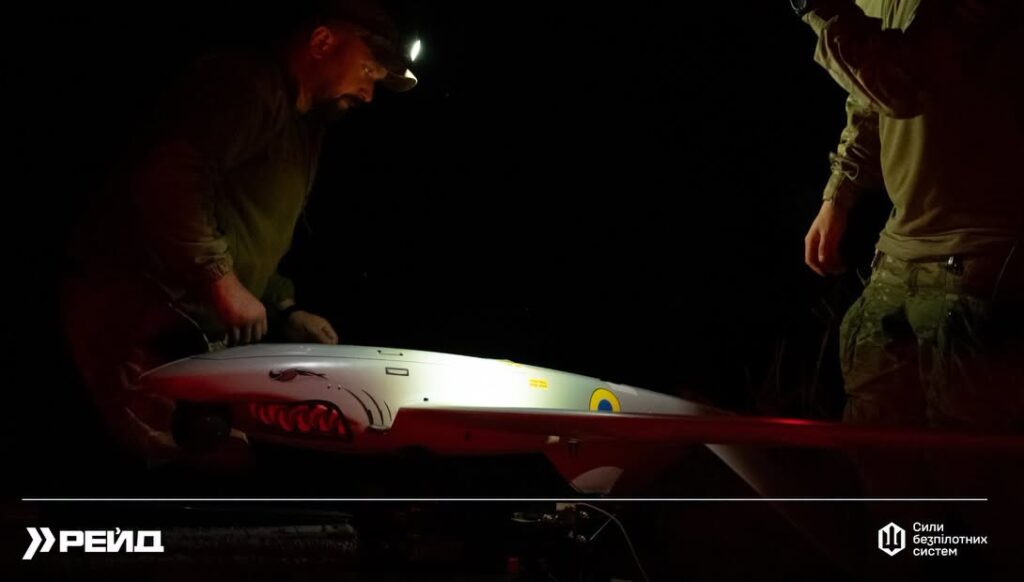 Two Ukrainian servicemembers prepare a fixed-wing reconnaissance drone on a launcher at night