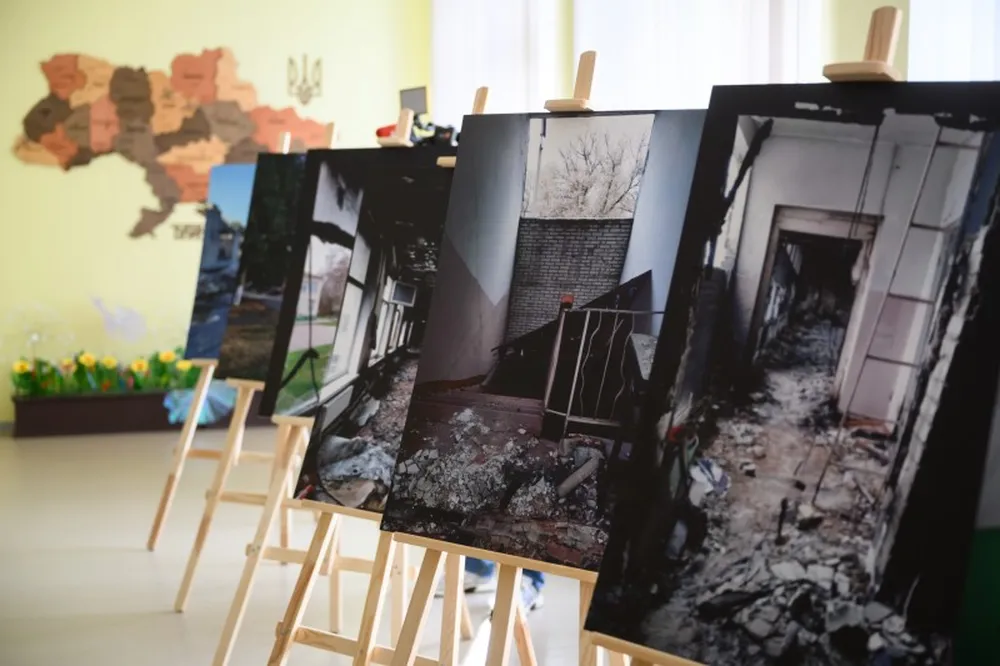 Photographs of burned and rubble-filled school interiors displayed on easels inside the rebuilt school.
