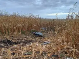 Scattered debris and a scorched patch of ground in a cornfield beneath a cloudy sky.